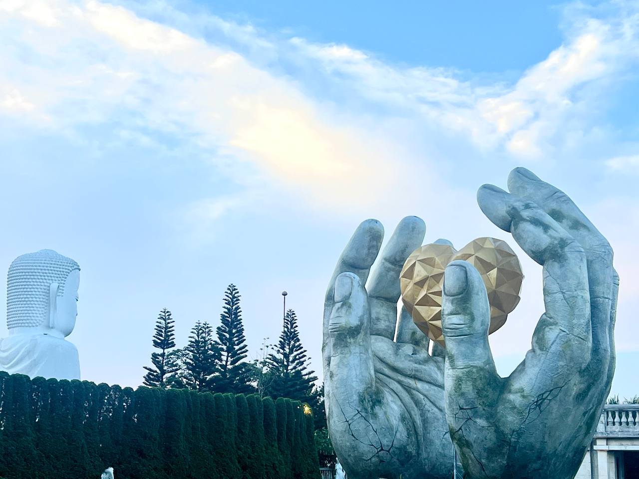 Giant stone hands holding a golden orb, with the white Buddha behind — Ba Na Hills